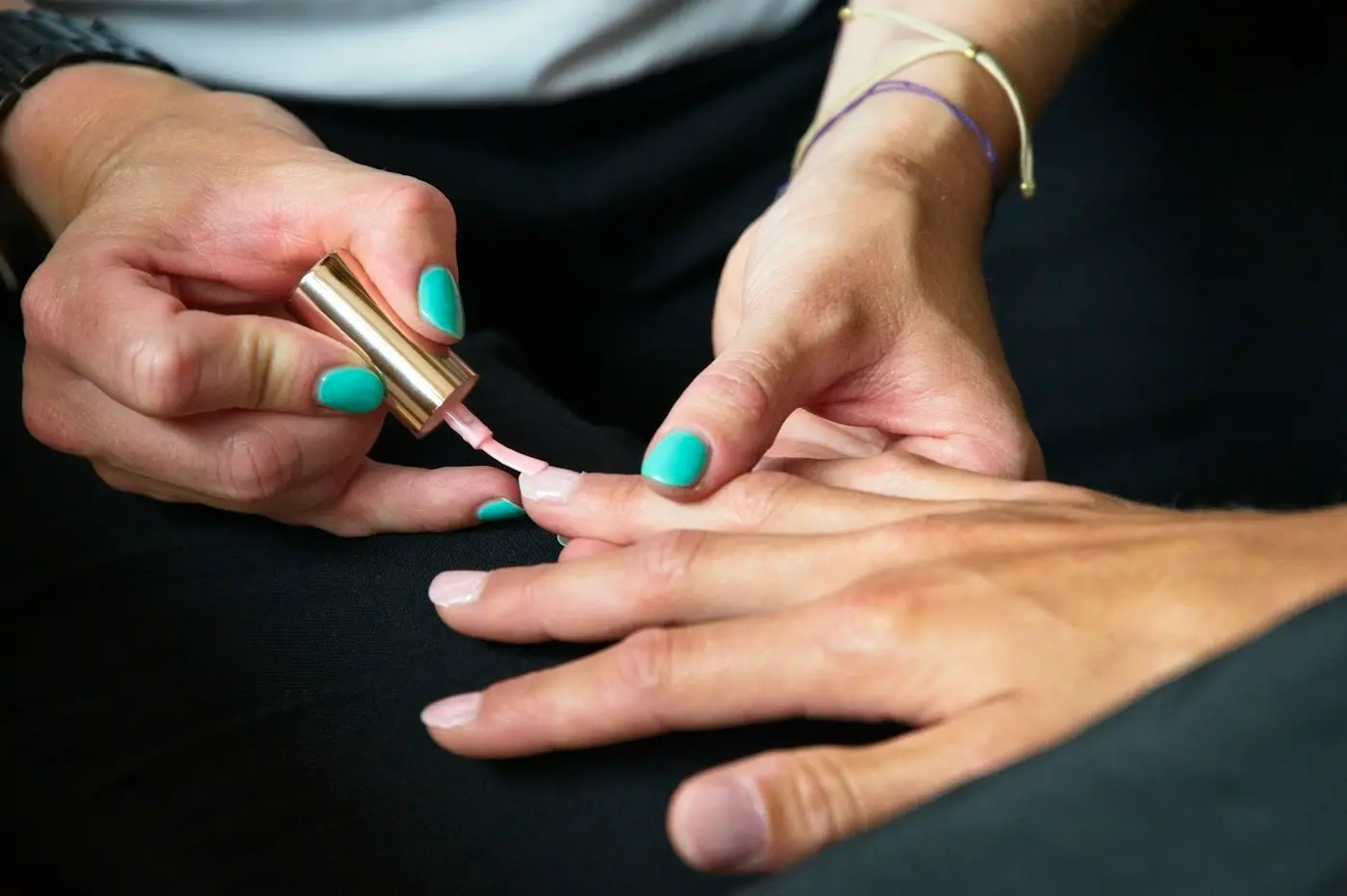 Manicure pintando as unhas de uma cliente com esmalte verde água
