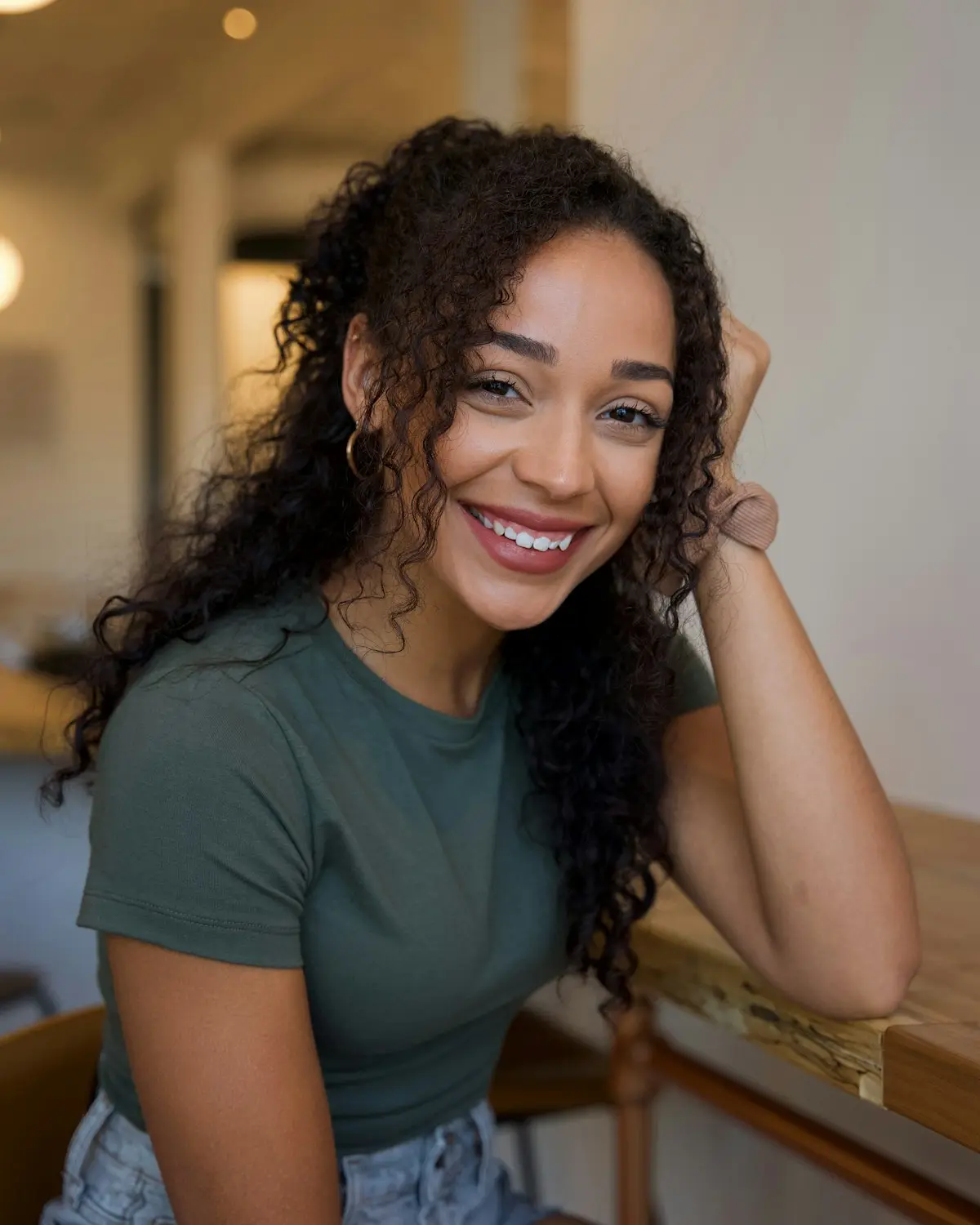 Mulher negra de cabelo cacheado sorrindo, com a mão no cabelo