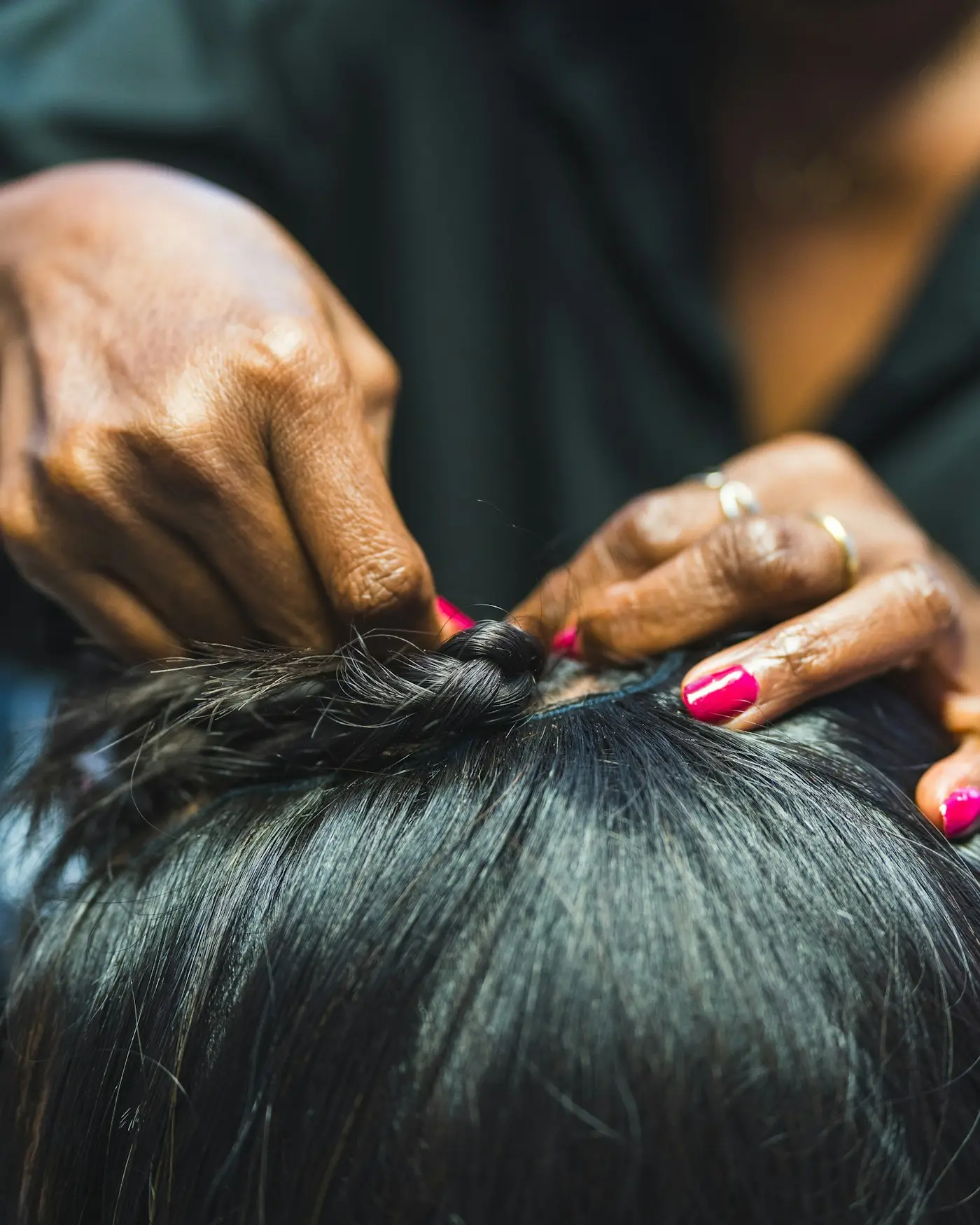 Mãos de uma trancista com unhas pintadas de rosa dividindo o cabelo crespo de uma cliente